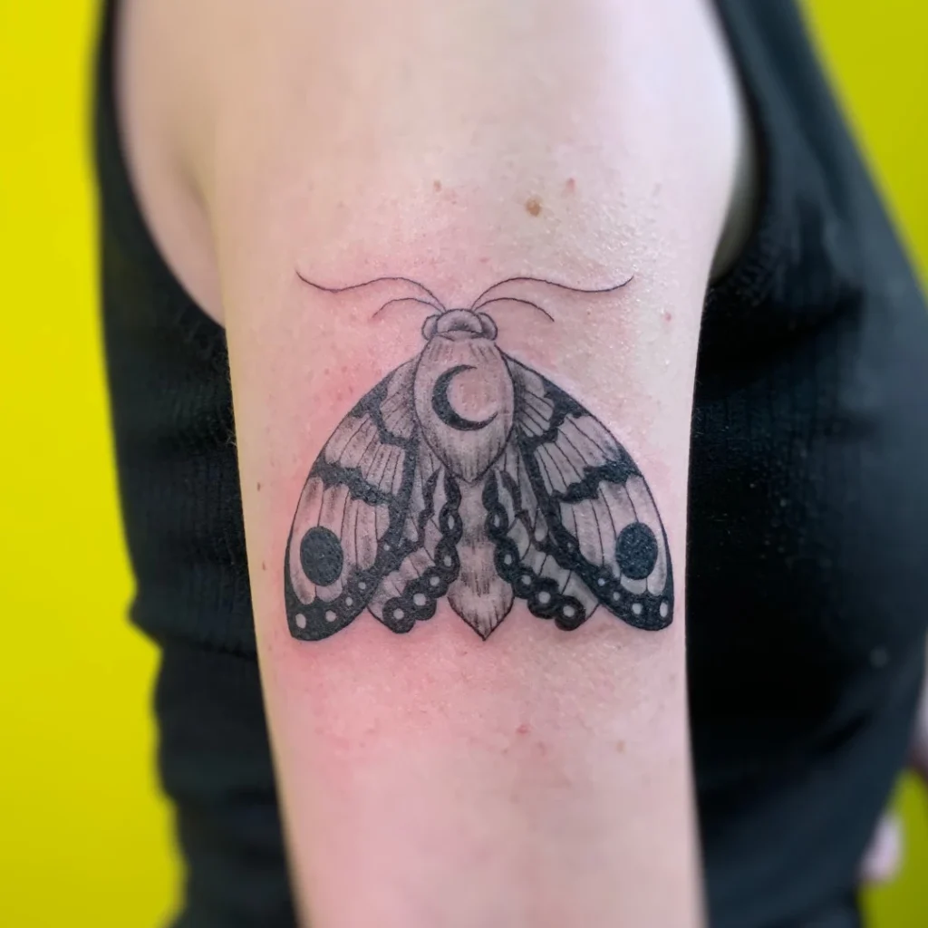 Black and grey bicep tattoo of a Moth with crescent moon on back