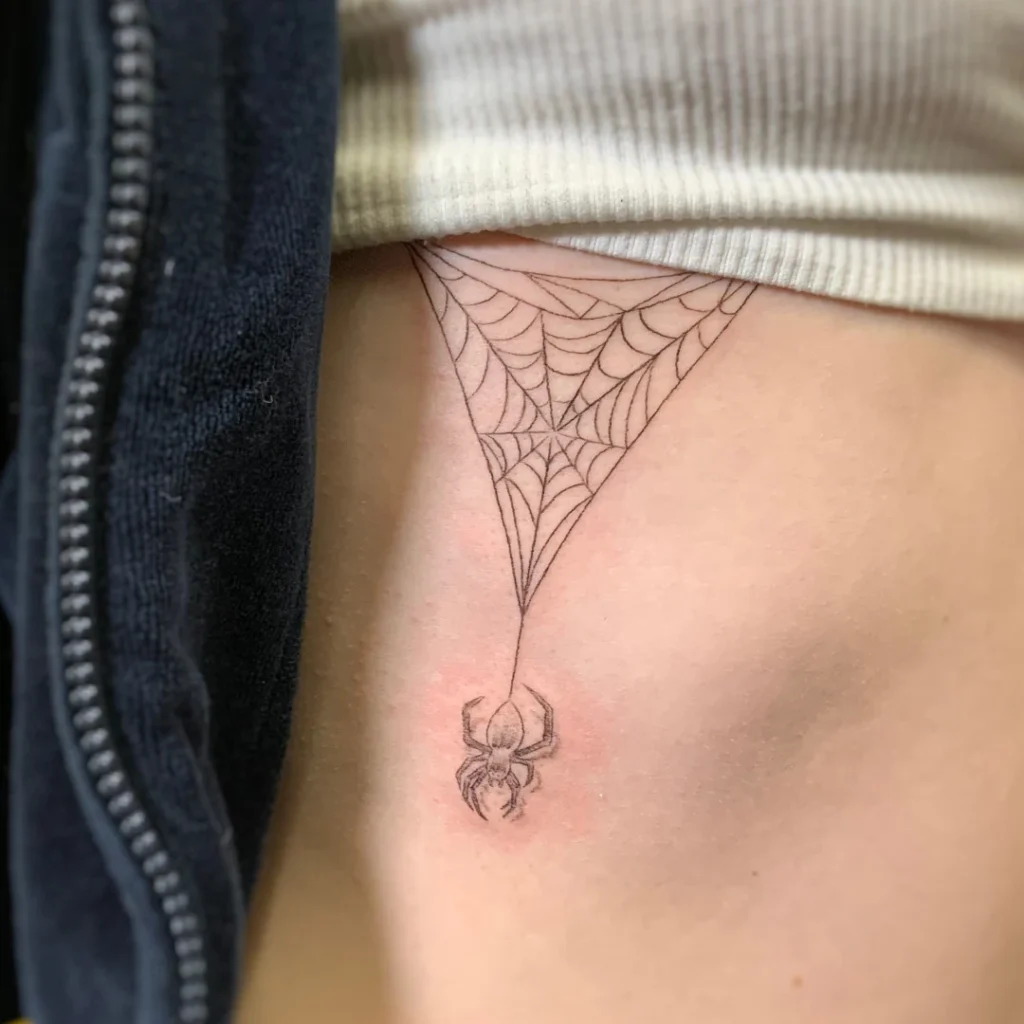 Fine line rib tattoo of a spider hanging from a web.