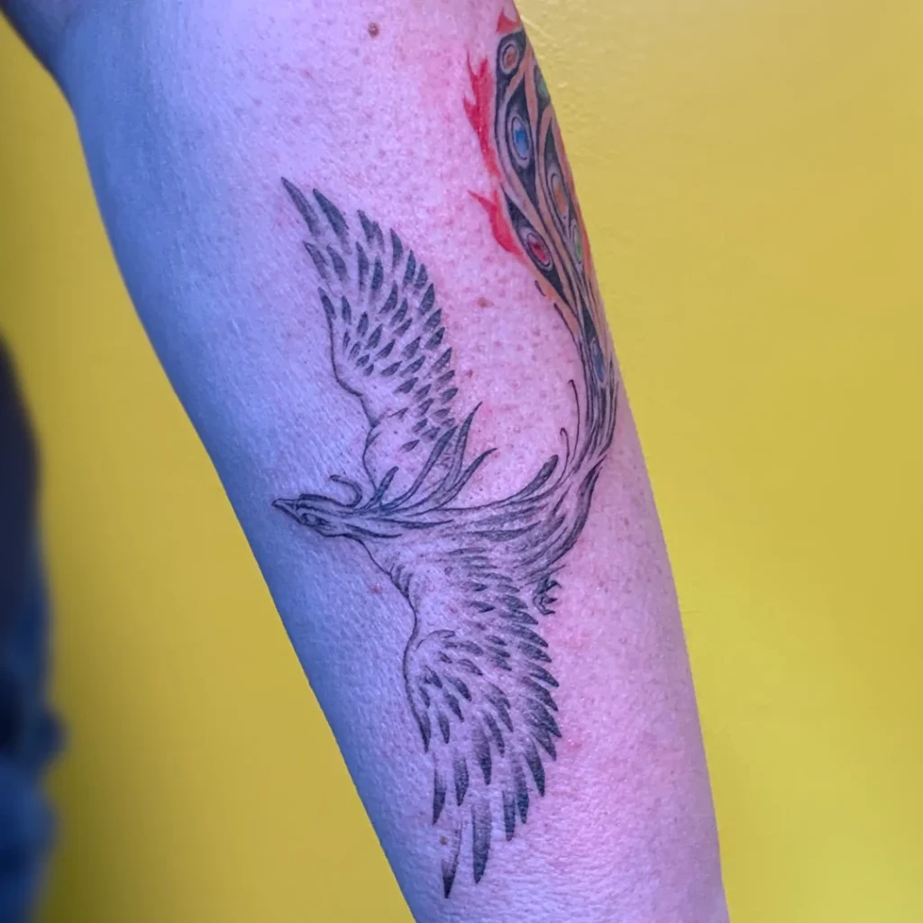 Forearm tattoo of a phoenix, rendered in black dotwork, with a full color tail ablaze.
