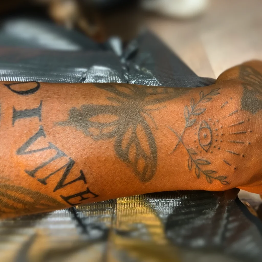 A forearm and wrist tattoo of the word "Divine" with a wavy effect working its way between two butterflies.