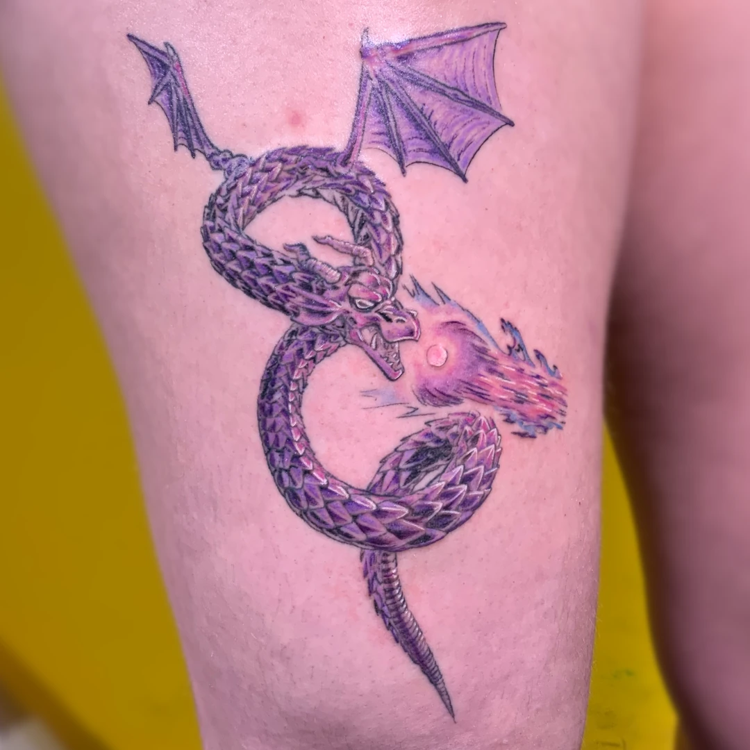 A thigh tattoo of a dragon shooting a beam of purple. Rendered in color.