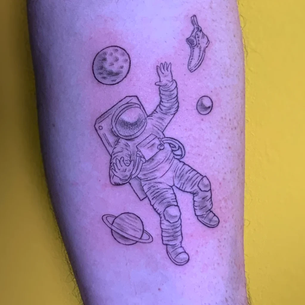A fine line arm tattoo of an astronaut surrounded by celestial objects, and the boot from monopoly.