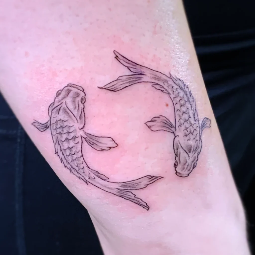 A forearm tattoo of two rotationally symmetrical koi, rendered in black and grey.