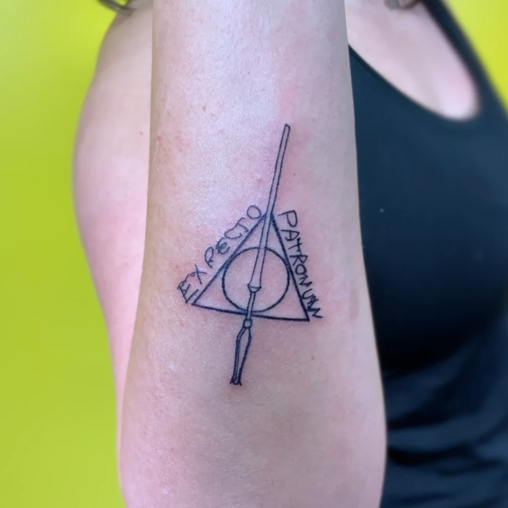 A forearm tattoo of the deathly hallows symbol with "expecto patronum" written in a family member's handwriting.