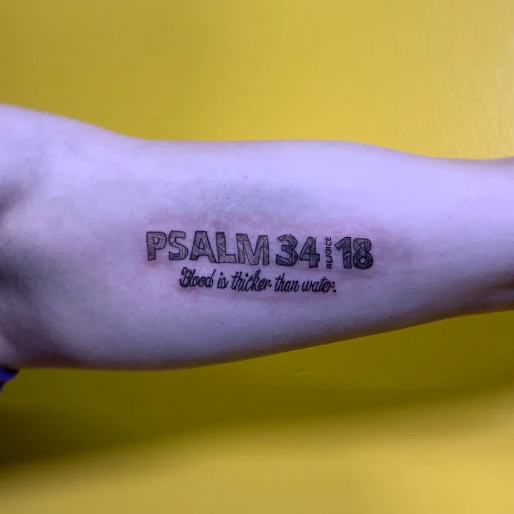 A tattoo of text in the middle of a bicep reading Psalm 34:18 Blood is thicker than water.